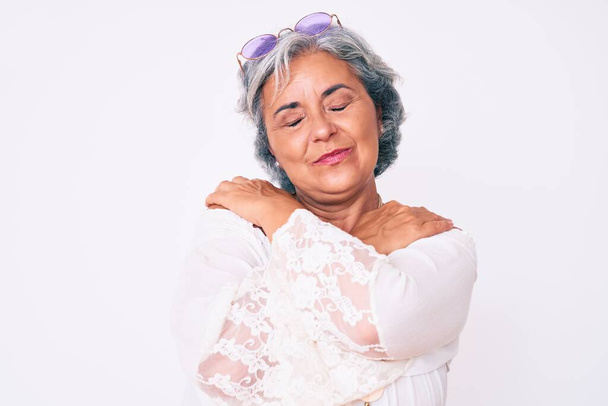 Ανώτερος ισπανόφωνη γκριζομάλλα γυναίκα φορώντας casual hippie ρούχα αγκαλιάζει τον εαυτό του ευτυχισμένη και θετική, χαμογελώντας αυτοπεποίθηση. αυτοαγάπη και αυτοφροντίδα  - Φωτογραφία, εικόνα