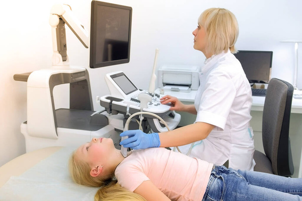 Doctor examining patient child girl thyroid gland using ultrasound scanner. - Фото, изображение