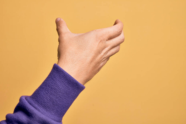 Ruka bělocha, mladý muž ukazující prsty na izolovaném žlutém pozadí, držící neviditelný předmět, prázdná ruka, která stříhá a chytá gesto - Fotografie, Obrázek