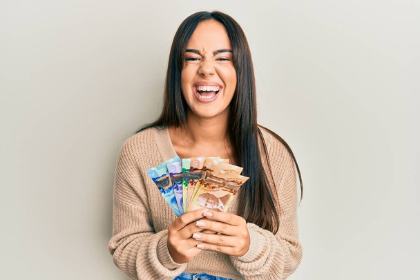 Young beautiful hispanic girl holding canadian dollars smiling and laughing hard out loud because funny crazy joke.  - Photo, Image