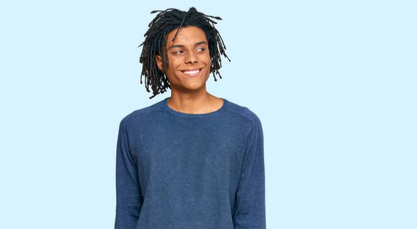 Молодий афроамериканець, одягнений у звичайний зимовий светр, дивиться убік з посмішкою на обличчі, природним виразом. сміючись.  - Фото, зображення