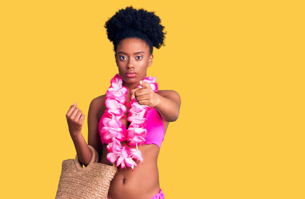 Joven mujer afroamericana vistiendo bikini y lei hawaiano señalando con el dedo a la cámara y a ti, gesto confiado mirando en serio  - Foto, Imagen