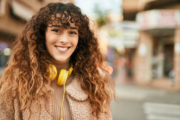 Jeune femme hispanique souriant heureux en utilisant des écouteurs à la ville - Photo, image