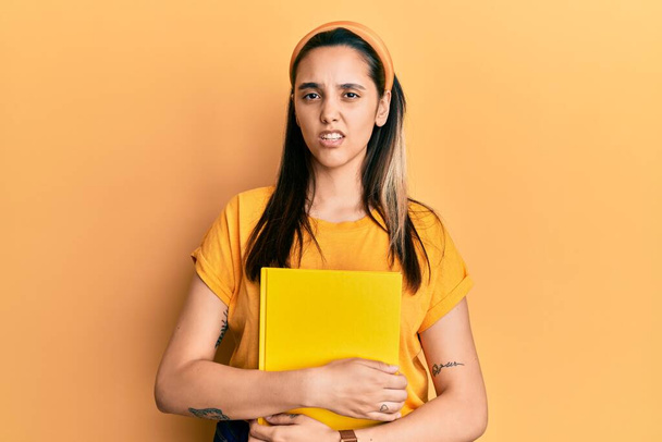Young hispanic woman wearing student backpack and holding book clueless and confused expression. doubt concept.  - Photo, image