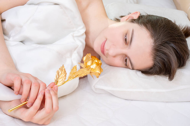 Birthday morning. Lying on the bed happy smiling girl holding a golden rose at home, front view. Can be used for wedding day, Christmas, Valentine's Day - Foto, immagini