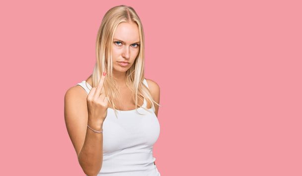 Young blonde girl wearing casual style with sleeveless shirt showing middle finger, impolite and rude fuck off expression  - Foto, imagen