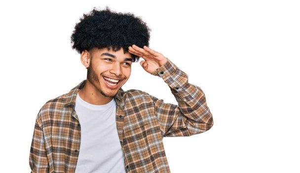 Young african american man with afro hair wearing casual clothes very happy and smiling looking far away with hand over head. searching concept.  - Fotografie, Obrázek