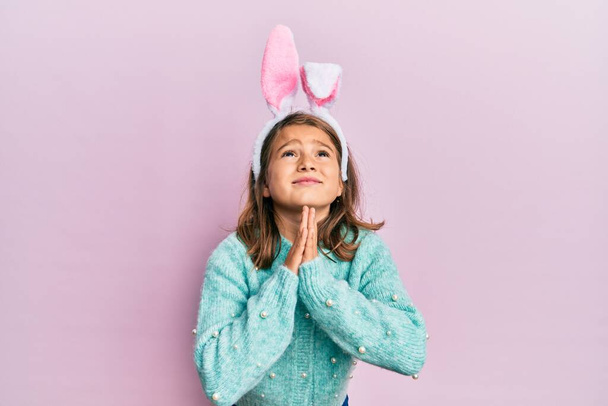 Malá krásná dívka na sobě roztomilé velikonoční zajíček uši prosit a modlit se s rukama dohromady s nadějí výraz na tváři velmi emocionální a ustaraný. žebrání.  - Fotografie, Obrázek