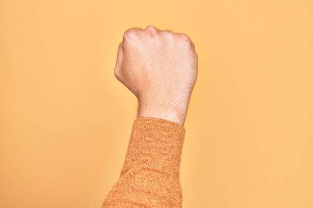 Рука кавказского юноши показывает пальцы на изолированном желтом фоне, делая протест и революционный жест, кулак выражая силу и силу - Фото, изображение