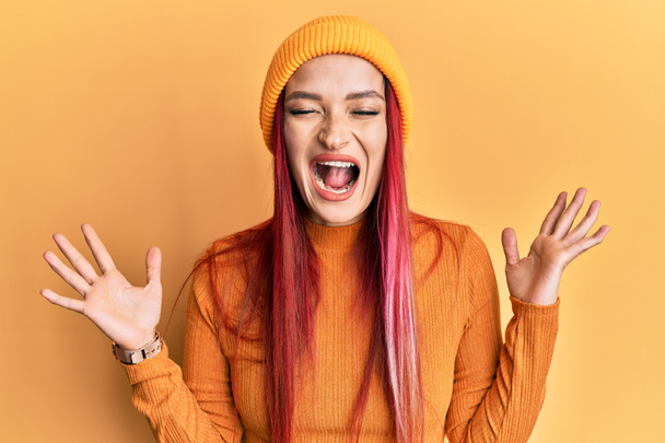 Young caucasian woman wearing wool cap celebrating mad and crazy for success with arms raised and closed eyes screaming excited. winner concept  - Fotoğraf, Görsel