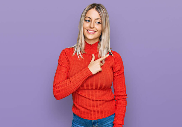 Beautiful blonde woman wearing casual clothes cheerful with a smile on face pointing with hand and finger up to the side with happy and natural expression  - Photo, Image