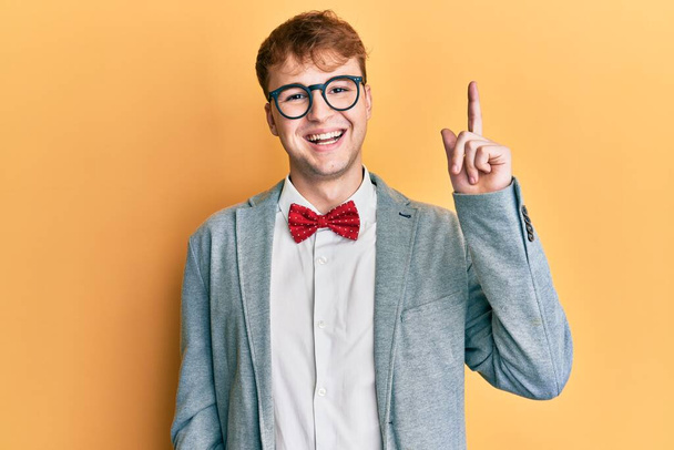 若い白人オタク男性は、成功したアイデアで指を指す蝶ネクタイでヒップスターエレガントな外観を身に着けている眼鏡をかけています。興奮して幸せよ。第1位.  - 写真・画像