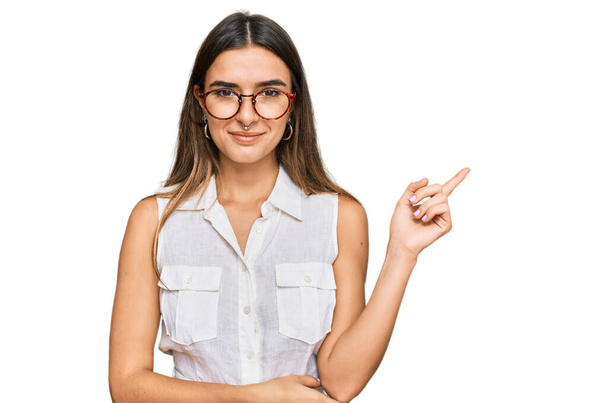 Молода іспаномовна жінка в повсякденному одязі усміхається щасливим вказуючи рукою і пальцем в бік
  - Фото, зображення