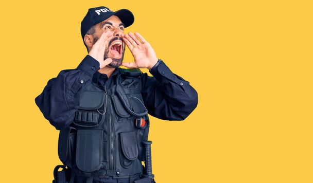 Junger hispanischer Mann in Polizeiuniform schreit wütend laut mit den Händen über dem Mund  - Foto, Bild