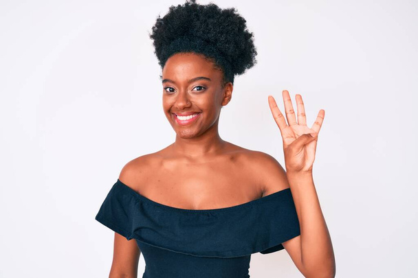 Genç Afro-Amerikalı kadın, günlük kıyafetler giyip dört numaralı parmaklarıyla işaret ederken kendinden emin ve mutlu bir şekilde gülümsüyor..  - Fotoğraf, Görsel