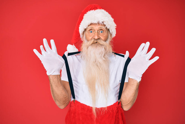 Old senior man wearing santa claus costume with suspenders celebrating crazy and amazed for success with open eyes screaming excited.  - Photo, Image