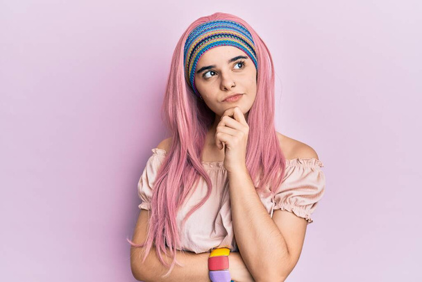 Fiatal latin lány rózsaszín hajjal gondolkodik koncentrált kétség ujjal az állán, és felnézett csodálkozva  - Fotó, kép