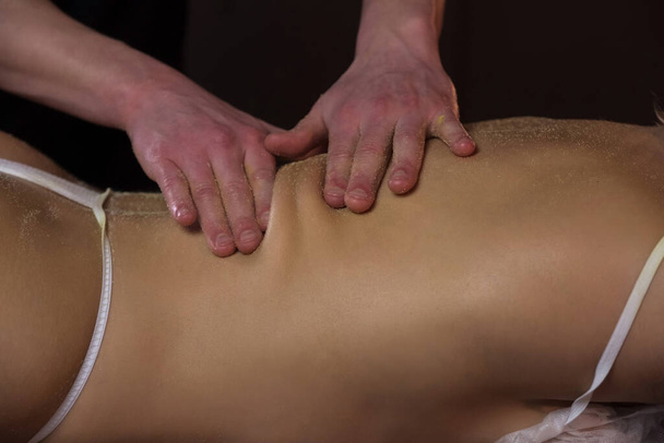 Massagist is scrubbing woman back with natural scrub in spa salon peeling body. - Фото, изображение