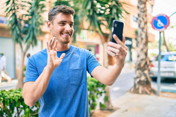 Νεαρός καυκάσιος άνδρας χαμογελά χαρούμενος κάνοντας βιντεοκλήση χρησιμοποιώντας smartphone στην πόλη. - Φωτογραφία, εικόνα