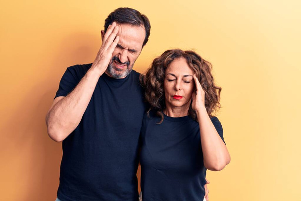 Moyen âge beau couple portant t-shirt debout sur fond jaune isolé avec la main sur la tête, maux de tête parce que le stress. Migraine souffrante. - Photo, image