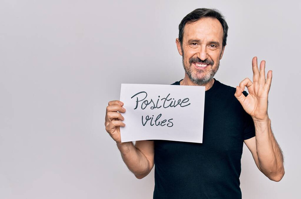 Middle age handosme man asking for good attitude holding paper with positive vibes message doing ok sign with fingers, smiling friendly gesturing excellent symbol - Photo, Image