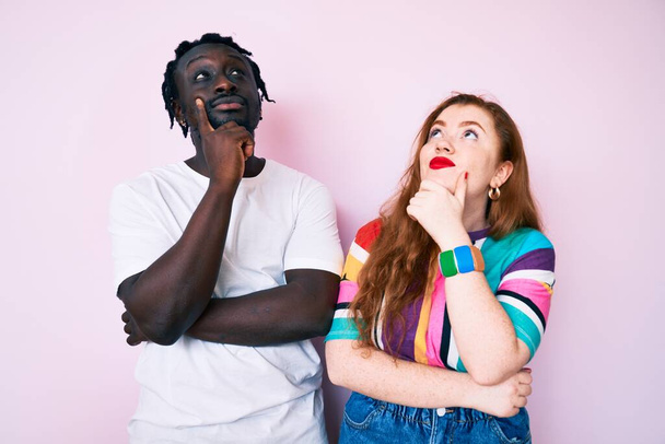 Interracial couple wearing casual clothes with hand on chin thinking about question, pensive expression. smiling and thoughtful face. doubt concept.  - Photo, Image