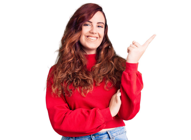 Mujer hermosa joven con suéter casual de invierno con una gran sonrisa en la cara, apuntando con la mano y el dedo hacia el lado mirando a la cámara.  - Foto, imagen