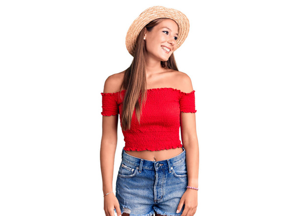 Young beautiful hispanic woman wearing summer hat looking away to side with smile on face, natural expression. laughing confident.  - Foto, Imagem