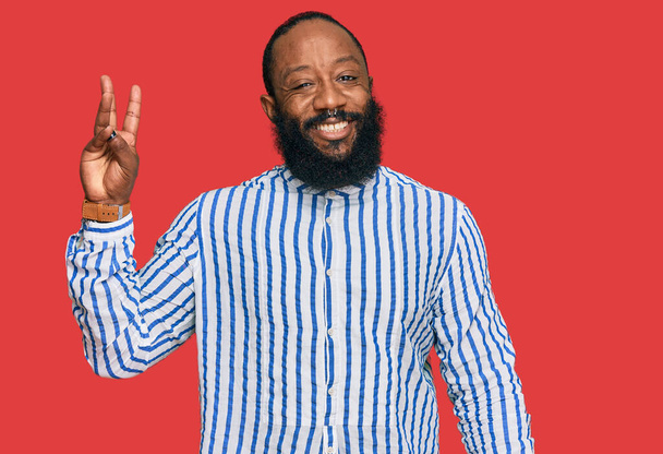 Jonge Afro-Amerikaanse man draagt zakelijke shirt tonen en wijzen met vingers nummer drie, terwijl glimlachen vol vertrouwen en gelukkig.  - Foto, afbeelding