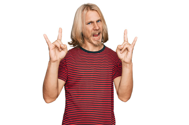 Caucasian man with blond long hair wearing casual striped t shirt shouting with crazy expression doing rock symbol with hands up. music star. heavy concept.  - Fotografie, Obrázek