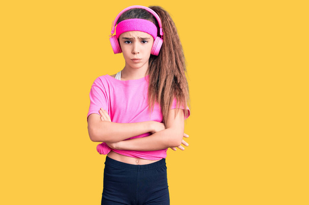 Cute hispanic child girl wearing gym clothes and using headphones skeptic and nervous, disapproving expression on face with crossed arms. negative person.  - Photo, Image