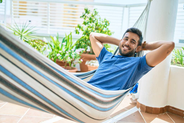 Молодий іспаномовний чоловік розслабився усміхнений щасливий лежить на гамаку на терасі
. - Фото, зображення