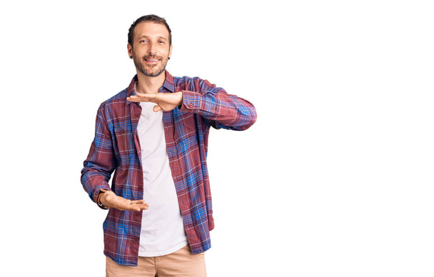 Young handsome man wearing casual clothes gesturing with hands showing big and large size sign, measure symbol. smiling looking at the camera. measuring concept.  - 写真・画像