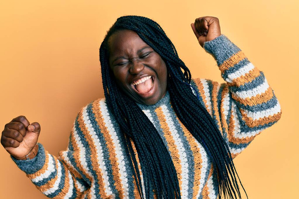 Jonge zwarte vrouw met vlechten dragen casual winter trui dansen gelukkig en vrolijk, glimlachen bewegend casual en zelfverzekerd luisteren naar muziek  - Foto, afbeelding