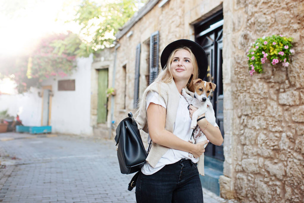 Образ жизни счастливой молодой женщины, гуляющей по старой городской улице с маленьким собачкой Джеком Расселом. Пьющий чай. Носит стильный минималистический наряд. Концепция свободы и счастья. Туризм и приключения - Фото, изображение