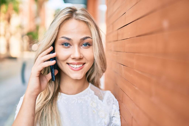 Jeune fille caucasienne souriant heureux parler sur le smartphone appuyé sur le mur. - Photo, image