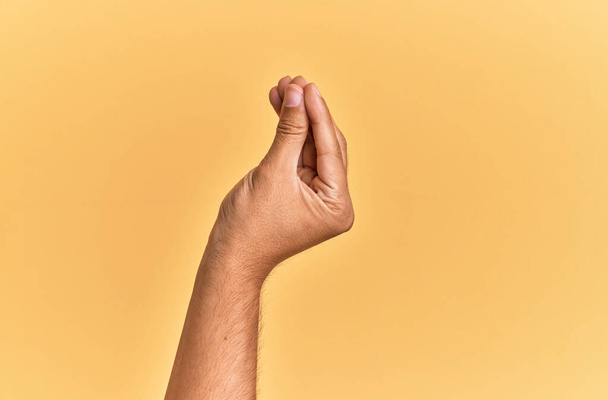 Χέρι και χέρι του καυκάσιου άνδρα πάνω από κίτρινο απομονωμένο φόντο κάνει ιταλική χειρονομία με τα δάχτυλα μαζί, κίνηση χειρονομία επικοινωνίας  - Φωτογραφία, εικόνα