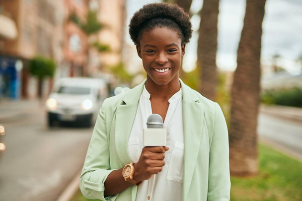 Joven reportera afroamericana usando micrófono en la ciudad - Foto, imagen