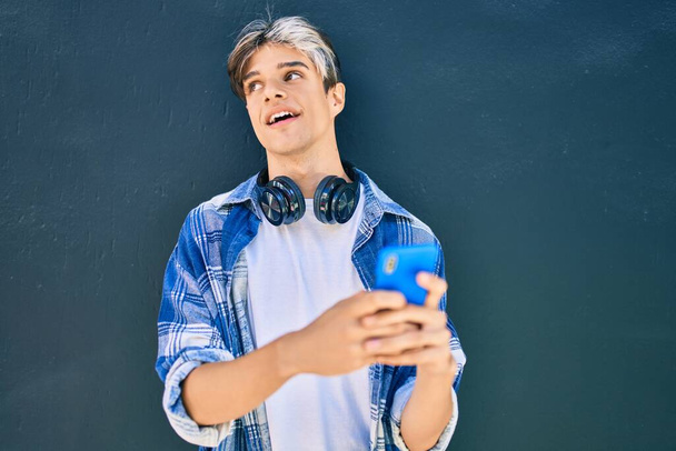 Giovane uomo ispanico sorridente felice con smartphone e cuffie in città. - Foto, immagini