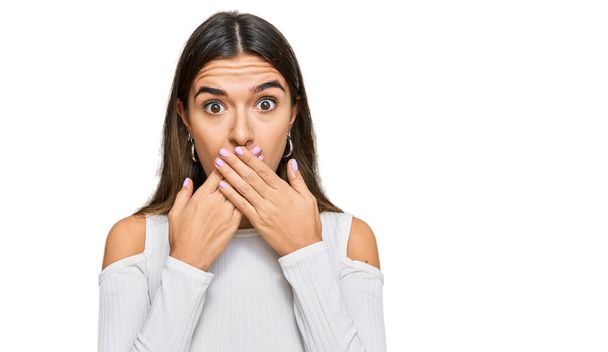 Junge hispanische Frau in lässiger Kleidung schockiert Mund mit Händen für Fehler bedeckt. Geheimes Konzept.  - Foto, Bild