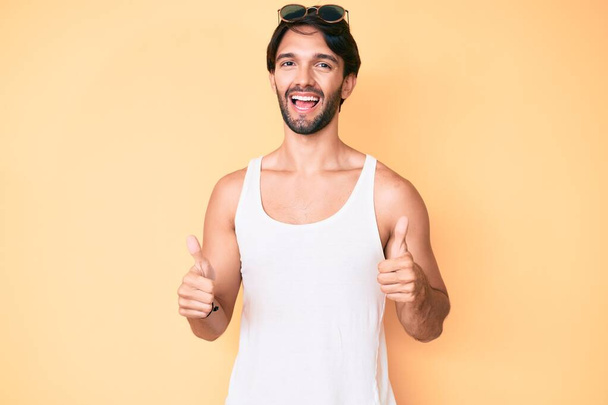 Handsome hispanic man wearing summer look and sunglasses success sign doing positive gesture with hand, thumbs up smiling and happy. cheerful expression and winner gesture.  - Photo, image