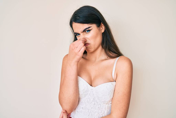 Bruneta dospívající dívka elegantně čichá k něčemu smradlavému a odpornému, nesnesitelnému, zadržuje dech s prsty na nose. špatný zápach  - Fotografie, Obrázek