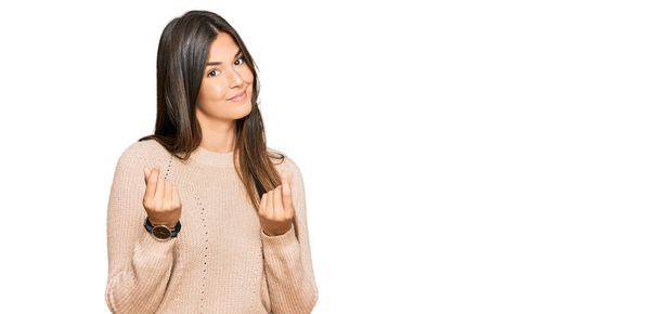 Young brunette woman wearing casual winter sweater doing money gesture with hands, asking for salary payment, millionaire business  - Фото, зображення