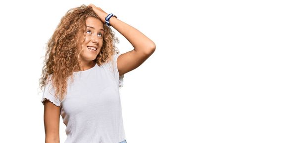 Belle adolescente caucasienne portant un t-shirt blanc décontracté souriant confiant touchant les cheveux avec geste de la main vers le haut, posant attrayant et à la mode  - Photo, image