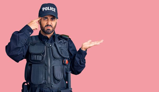 Jovem hispânico vestindo uniforme policial confuso e irritado com a palma aberta mostrando espaço de cópia e apontando o dedo para a testa. Pense nisso..  - Foto, Imagem