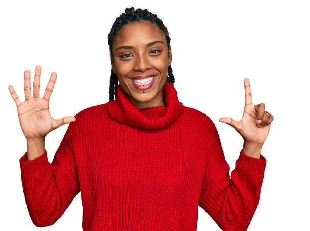 Femme afro-américaine portant un pull d'hiver décontracté montrant et pointant vers le haut avec les doigts numéro sept tout en souriant confiant et heureux.  - Photo, image