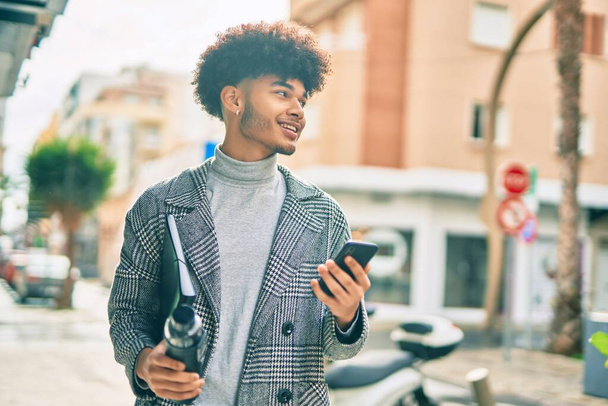 Nuori afrikkalainen amerikkalainen liikemies, joka käyttää älypuhelinta pitämällä vesipulloa kaupungissa. - Valokuva, kuva