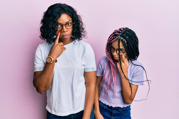 Bella afro-americana madre e figlia indossa abiti casual e occhiali che puntano verso l'occhio che ti guarda gesto, espressione sospetta  - Foto, immagini