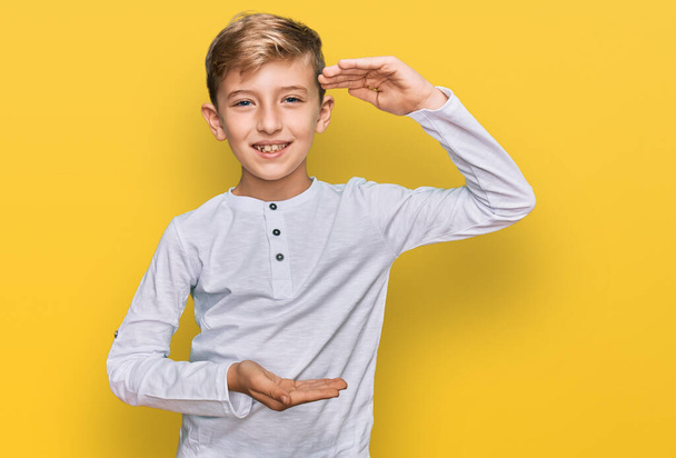 Malý kavkazský chlapec v neformálním oblečení, gestikulující rukama s velkým a velkým znakem velikosti, symbol míry. s úsměvem na kameru. koncepce měření.  - Fotografie, Obrázek