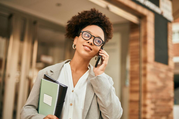 Joven mujer de negocios afroamericana sonriendo feliz hablando en el teléfono inteligente de la ciudad. - Foto, Imagen
